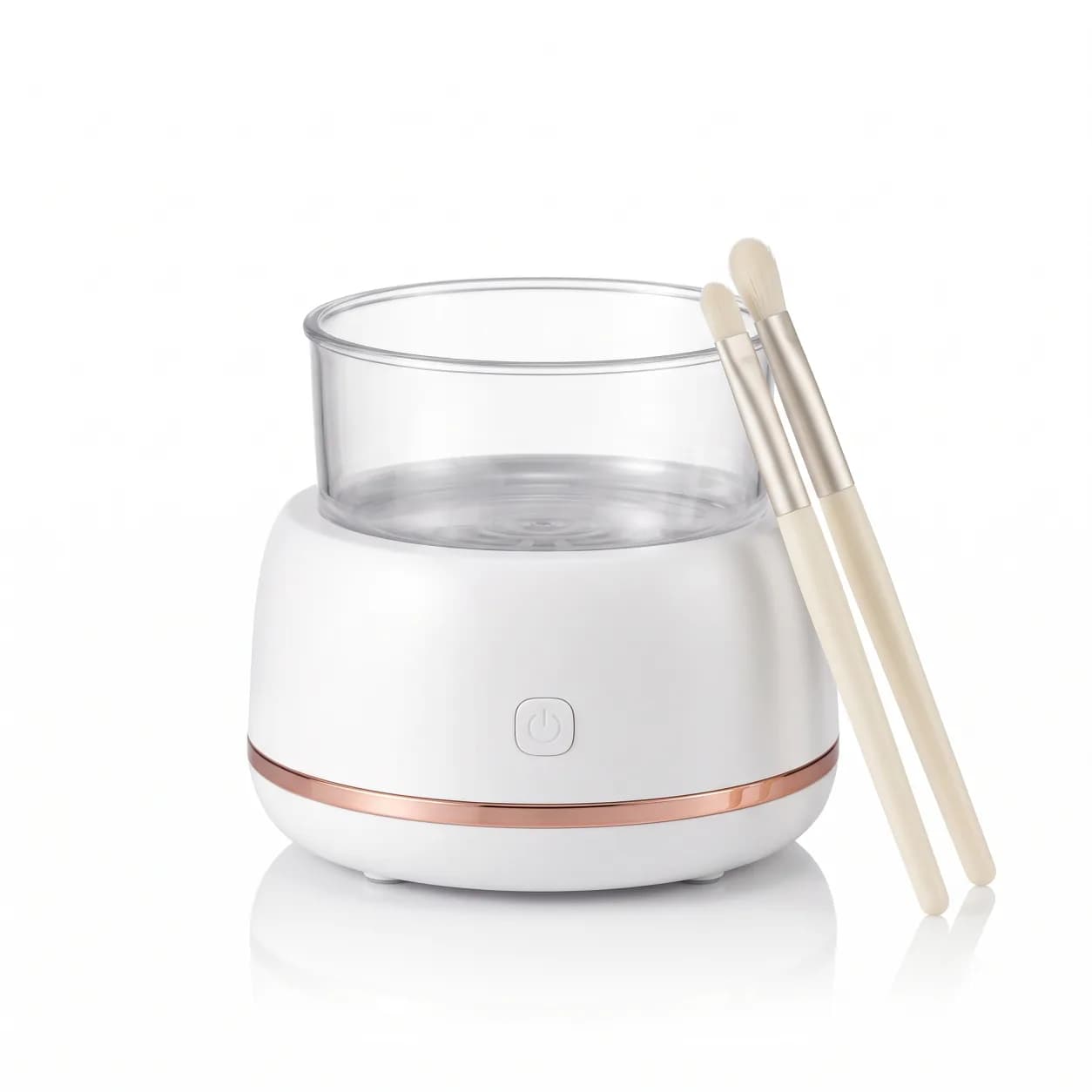 White electric makeup brush cleaner with clear washing bowl and two cream-handled makeup brushes